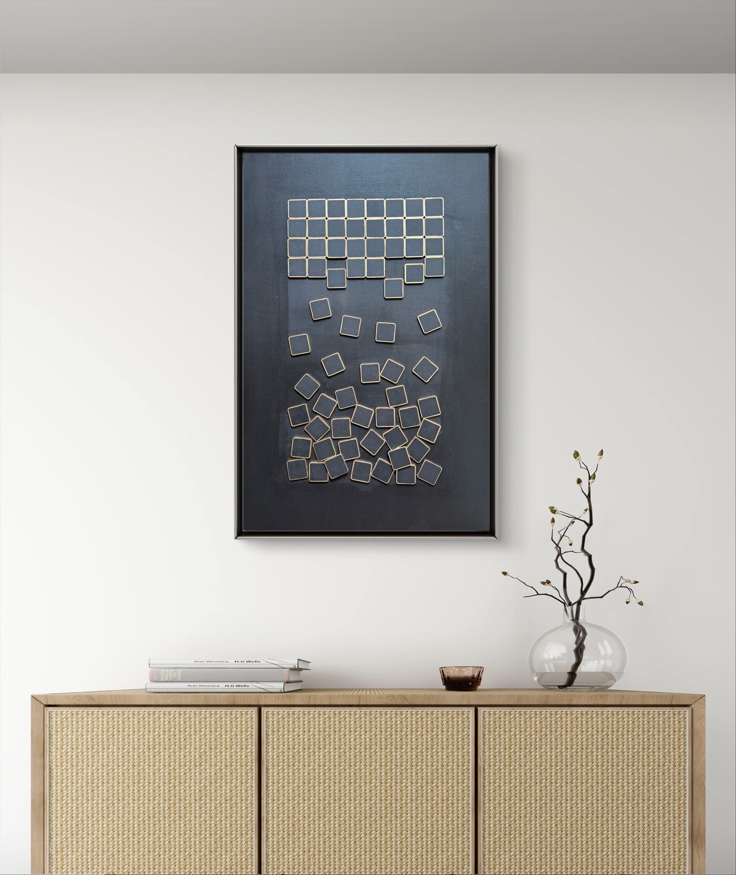 Framed abstract art piece on a wall above a wooden cabinet.