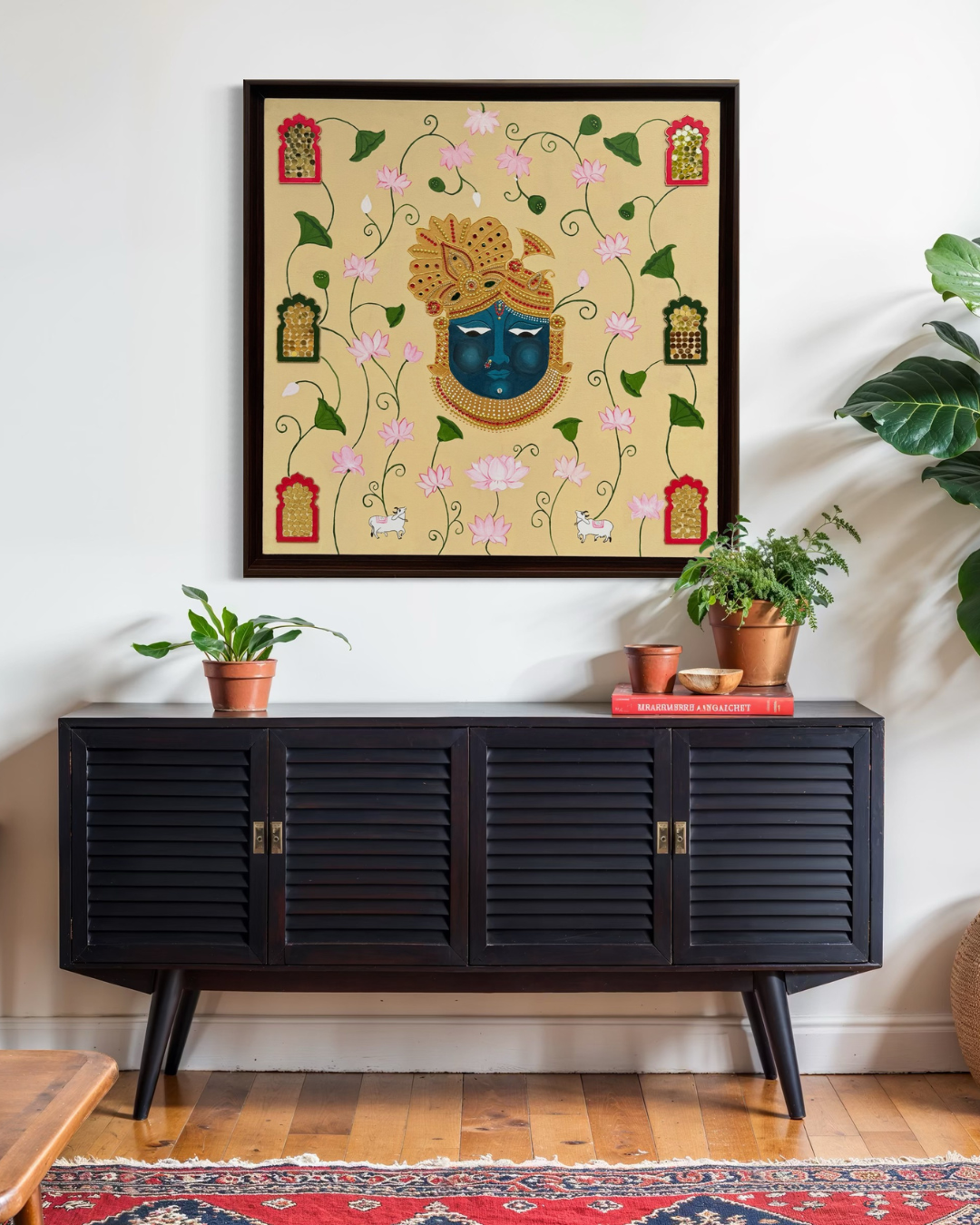 Hand-painted artwork of Lord Krishna’s face in blue with golden embellishments, surrounded by blooming pink lotus flowers, sacred cows, and decorative jaali window designs on a beige background.