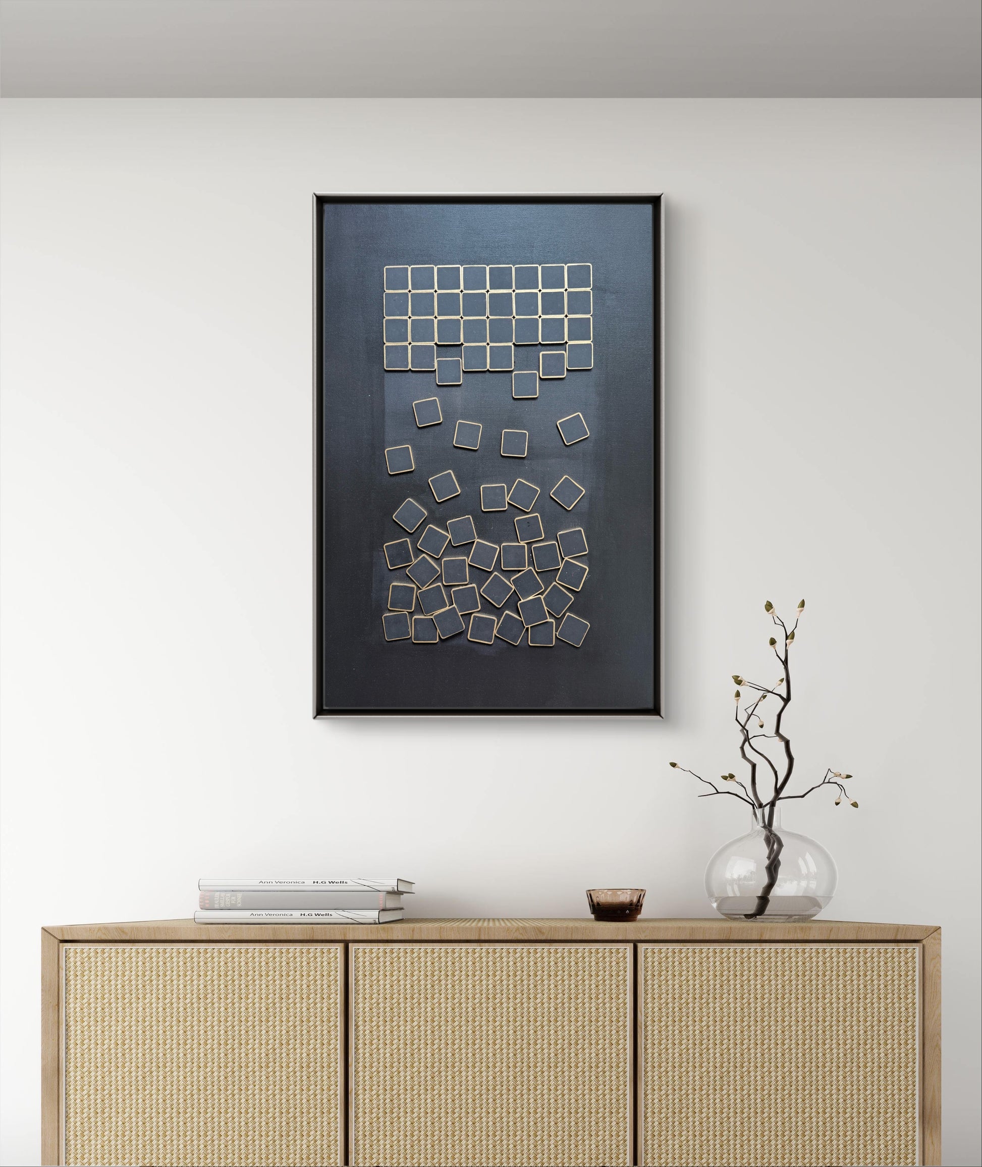 Framed abstract art piece on a wall above a wooden cabinet.